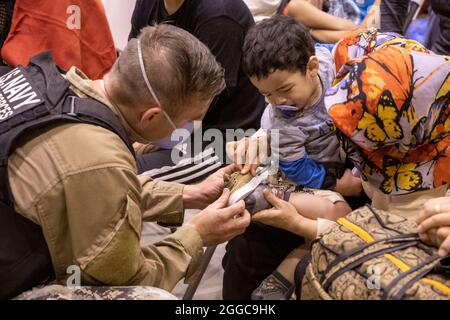 MARINESTÜTZPUNKT ROTA, Spanien (Aug 29, 2021) EIN Seemann aus der Naval Station (NAVSTA) Rota passt einem Kind, das nach der Ankunft seiner Familie in NAVSTA Rota am 29. August 2021 aus Afghanistan evakuiert wurde, ein neues Paar Schuhe an. NAVSTA Rota unterstützt derzeit die Mission des Außenministeriums, um die sichere Ausreise und Umsiedlung von US-Bürgern, Empfängern von Sondervisa für Immigration und gefährdeten Bevölkerungsgruppen aus Afghanistan zu erleichtern. (USA Navy Foto von Mass Communication Specialist 1st Class Nathan Stockfoto