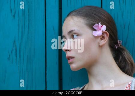 Porträt eines schönen Mädchen mit rosa Blume hinter dem Ohr gegen den blau türkisfarbenen Holz strukturierten Hintergrund. Stockfoto