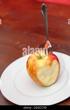 Vertikale Nahaufnahme einer Gabel in einem roten Apfel mit einer Seite in Form eines Herzzeichens Stockfoto