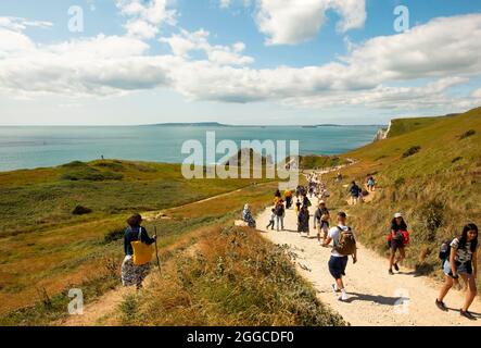 Menschen, die den Fußweg hinunter zur Durdle Door gehen, der ikonischsten Landschaft der Jurassic Coast mit ihrem natürlichen Kalksteinbogen. Dorset, Großbritannien. August 2021 Stockfoto