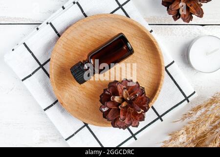 Ätherische Ölflasche auf einem Holztablett. Umweltfreundliches, trendiges Kosmetikkonzept. Kiefernessenz auf weißem Hintergrund. Stockfoto