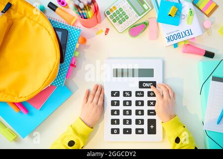 Zurück zur Schule. Obere Ansicht des modernen Kindes mit Arbeitsbüchern, Schreibwaren, Lehrbuch, Taschenrechner und Rucksack am weißen Tisch zu Hause. Stockfoto