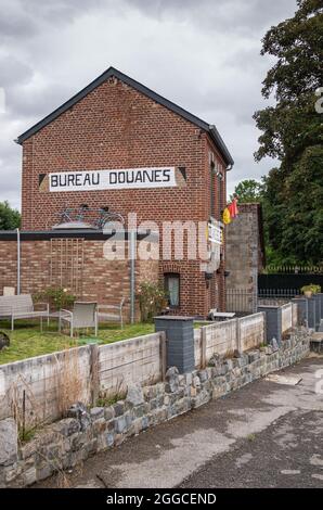 Hastière, Heer, Wallonien, Belgien - 10. August 2021: Historisches belgisches Zollbüro in rotem Backstein an der Grenze zu Frankreich mit Flagge unter g Stockfoto