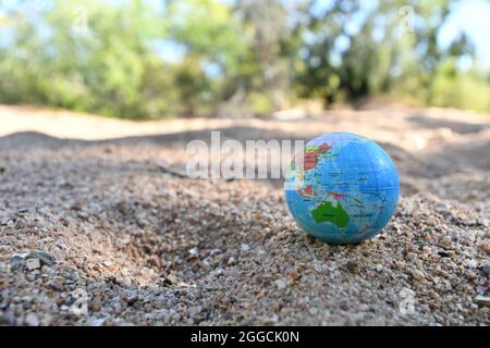 Erdkugel auf Flusssand mit Kreeksandtress entlang des Wasserlaufs im Hintergrund. Stockfoto