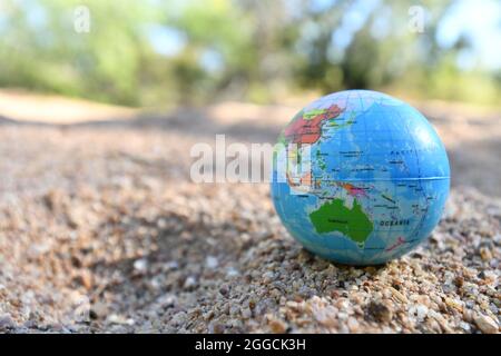 Erdkugel auf Flusssand mit Kreeksandtress entlang des Wasserlaufs im Hintergrund. Stockfoto