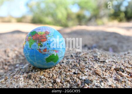 Erdkugel auf Flusssand mit Kreeksandtress entlang des Wasserlaufs im Hintergrund. Stockfoto