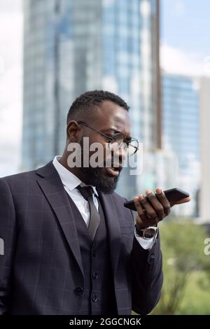 Zeitgemäßer Geschäftsmann, der Sprachnachrichten aufzeichnet, während er das Smartphone am unteren Gesichtsbereich hält Stockfoto