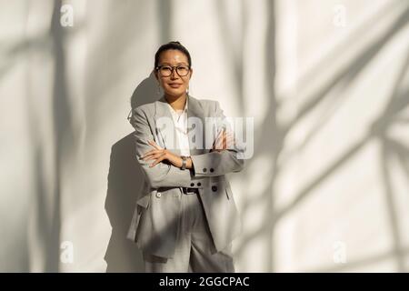 Junge asiatische Mitarbeiterin in elegantem Anzug, die ihre Arme an der Brust kreuzt Stockfoto