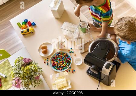 Zwei fröhliche männliche Kinder kochen hausgemachtes Backdessert zusammen Zutaten für Teig mischen Stockfoto