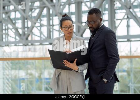 Zwei junge, selbstbewusste Makler diskutieren bei einem Arbeitstreffen in einem großen, modernen Business Center über Finanzpapiere Stockfoto
