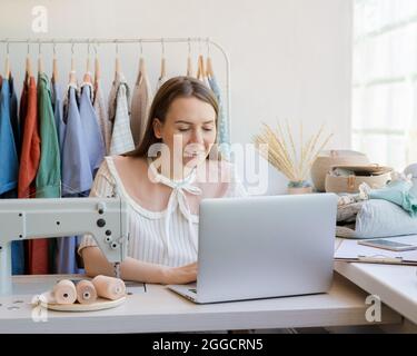 Weibliche Modedesignerin, die online Kleidungsdesign kreiert, während sie am Arbeitsplatz mit der Nähmaschine sitzt Stockfoto