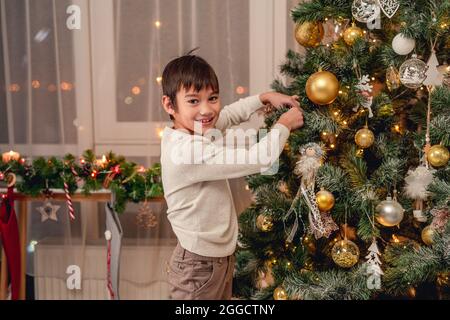 Lächelnder Junge hängt Ball auf weihnachtsbaum Stockfoto