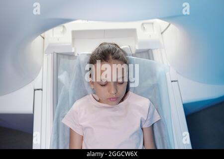 Blick auf das kleine Mädchen, das die Augen geschlossen hält, bevor es sich einer CT-Untersuchung in modernen Kliniken unterziehen muss Stockfoto