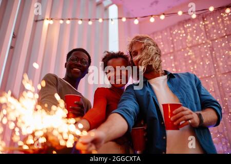 Porträt verschiedener Freunde, die Lichter an die Kamera halten, während sie in Innenräumen Party machen und Platz kopieren Stockfoto