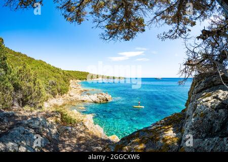 Atemberaubende Landschaft mit einer Person, die auf einem türkisfarbenen Wasser Stand-Up-Paddleboarding (SUP) macht. Porto Rotondo, Sardinien, Italien. Stockfoto