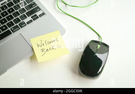 Willkommen zurück mit Smiley geschrieben auf gelbem Papierstock auf der Tastatur neben Computer-Maus. Stockfoto