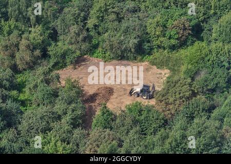 Der Bagger bereitet den Boden auf dem Feld im Wald unter den Bäumen für die Landschaftsgestaltung und Landwirtschaft, Draufsicht Stockfoto