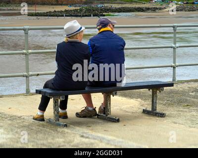 Mann und Frau genießen eine Pause auf einer Bank mit Blick auf das Meer bei Skinningrove Stockfoto
