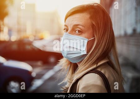 Schöne kaukasische Frau trägt medizinische Schutzmaske in der Stadt Straße. Porträt einer Frau aus dem Tausendjahrtausend. Soziale Distanz und Schutz vor Coronavirus Stockfoto