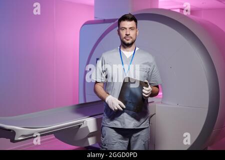 Junger erfolgreicher Radiologe mit Röntgenbild, das in Kliniken gegen mrt-Scan-Geräte steht Stockfoto
