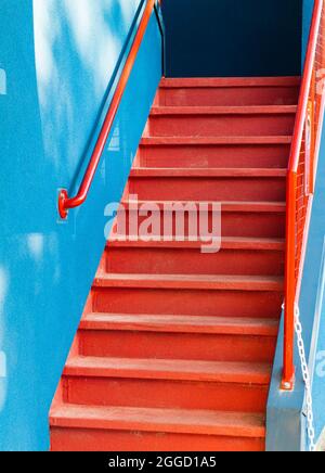 Eine leuchtend rote Holztreppe an der Seite einer blauen Wand des Hauses. Straßenansicht, Reisefoto, selektiver Fokus. Stockfoto