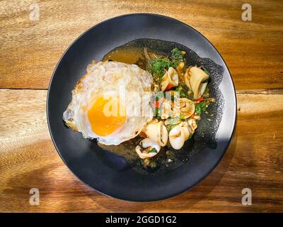 Reis mit gebratenem Tintenfisch und Basilikum mit gebratenem Ei gekrönt Stockfoto