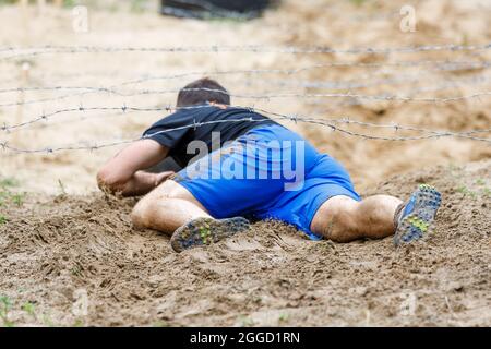 Der Sportler krabbelt im Hindernislauf unter einem Stacheldraht-Hindernis auf seinem Kurs Stockfoto