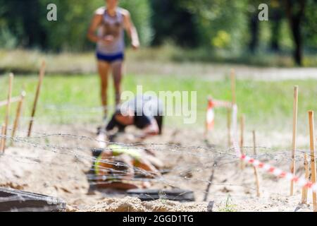 Sportler, die im Hindernislauf unter einem Stacheldraht-Hindernis auf ihrem Kurs krabbeln Stockfoto