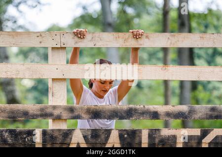 Junge Sportlerin klettert auf ihrem Hindernislauf durch die Holzwand Stockfoto