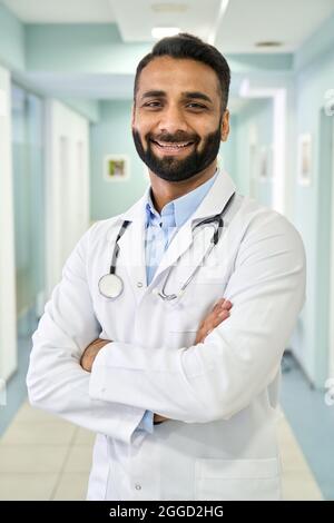 Vertikales Porträt eines glücklichen indischen Arztes, der im Klinikkrankenhaus steht. Stockfoto