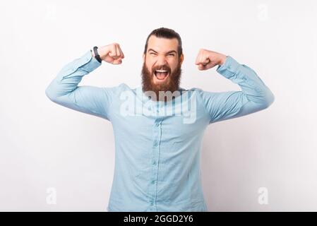 Selbstbewusster bärtiger Geschäftsmann hält die Arme hoch und macht die Machtgeste über weißem Hintergrund. Stockfoto