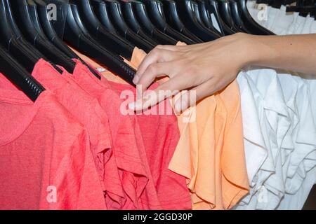 Ein Shopper pflückt T-Shirts auf Kleiderbügeln in einer Boutique. Nachhaltiges Leben und intelligenter Konsum. Verkauf von Kleidung in Geschäften und Online-Konzept. Meere Stockfoto