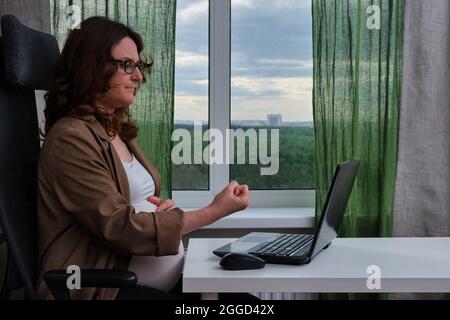 Schwanger Frau mit Laptop im Heimbüro zeigt Faust Stockfoto