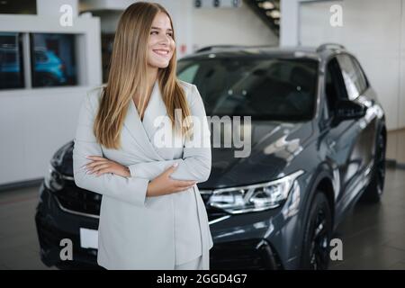 Porträt des Verkäufers im Autosalon. Attraktive junge Frau stend vor dem Auto Stockfoto