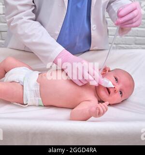 Der Arzt entfernt bei einem Neugeborenen eine laufende Nase mit einer Absaugvorrichtung. Krankenschwester in Uniform behandelt Kindernase für Grippe Stockfoto