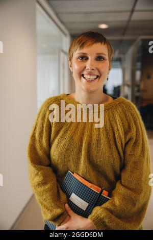 Fröhlicher Unternehmer, der im Amt steht. Geschäftsfrau in Casuals lächelt in die Kamera. Stockfoto
