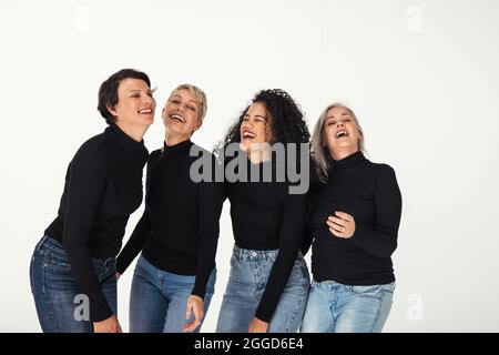 Fröhliche Gruppe von verschiedenen Frauen, die ihr Leben in einem Studio feiern. Vier körperpositive Frauen unterschiedlichen Alters lächeln fröhlich, während sie Jeans aga tragen Stockfoto
