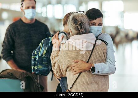 Mutter umarmt ihre Tochter und ihren Enkel am Ankunftseingang des Flughafens. Frau mit ihrem Sohn umarmte ihre Mutter am Flughafen in einer Pandemie. Stockfoto