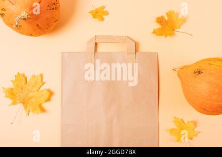 Einkaufstasche aus braunem Öko-Papier neben Kürbissen und Herbstblättern auf orangefarbenem Hintergrund, flach liegend. Stockfoto