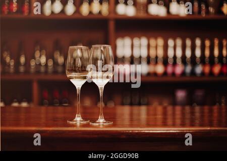 Zwei Gläser Weißwein auf dem hölzernen Bartisch. Fotos in warmen Farben. Konzentrieren Sie sich auf das Glas Wein. Valentinstag, Datum, Liebe, Feier Stockfoto