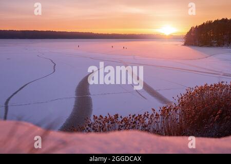 Familien-Silhouette von vier Personen Eiskunstlauf am gefrorenen See gegen schönen Sonnenuntergang. Aktivitäten im Freien an Wochenenden bei kaltem Wetter. Stockfoto