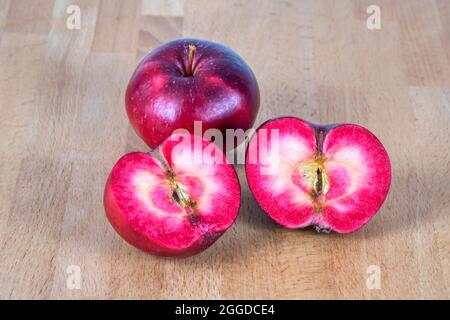Rote fleischige Äpfel auf dem Tisch, einer in Scheiben geschnitten, um die Farbe des roten Fleisches im Inneren zu zeigen. Stockfoto