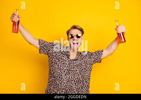 Foto von ziemlich charismatischen jungen Gentleman gekleidet drucken Hemd dunkle Gläser halten zwei Bierflaschen isoliert gelben Hintergrund Stockfoto