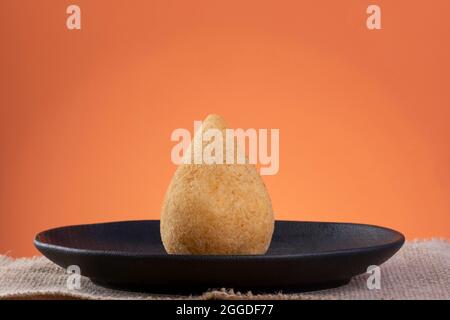 Gebratener Coxinha auf einem schwarzen Teller mit orangefarbenem Hintergrund. Stockfoto