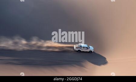 Ein weißer Pickup-Truck fährt von einer Sanddüne hoch und spritzt Sand in die Luft und um in Dasht e lut oder sahara Wüste. ADS Raum Stockfoto