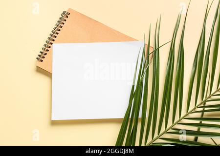 Leere Karte, Notizbuch und Palmblatt auf farbigem Hintergrund Stockfoto
