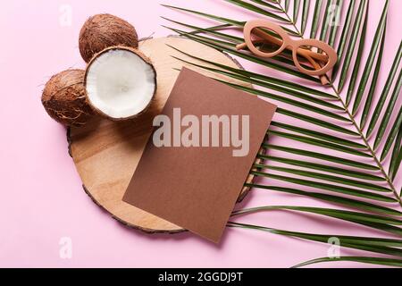 Komposition mit leerer Karte, Kokosnüssen, Sonnenbrille und Palmblatt auf farbigem Hintergrund Stockfoto