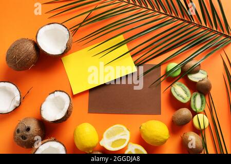 Komposition mit leeren Karten, Früchten und Palmblatt auf farbigem Hintergrund Stockfoto