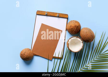 Komposition mit leerer Karte, Klemmbrett und reifen Kokosnüssen auf farbigem Hintergrund Stockfoto