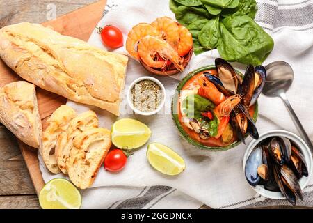 Schüssel mit leckerer Cacciucco-Suppe und Zutaten auf Holzboden Stockfoto